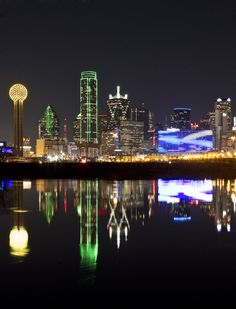 the city skyline is lit up at night with lights reflecting in the water on the surface