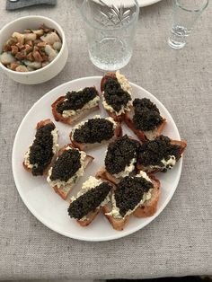 a white plate topped with toasted sandwiches covered in black cauliflower and cream cheese