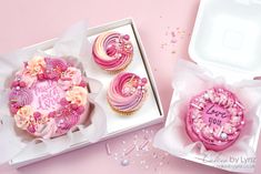 two decorated cupcakes in pink and white boxes