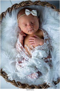 a newborn baby wearing a white lace outfit and laying in a wicker basket with feathers