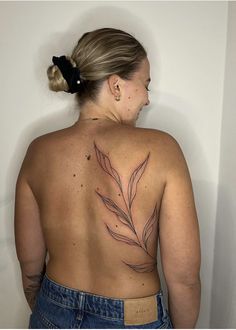 a woman with a tattoo on her back is standing in front of a white wall