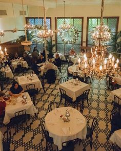 people sitting at tables in a restaurant with chandeliers hanging from the ceiling and windows