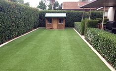 an artificial lawn in a back yard with a shed and bushes behind it, surrounded by shrubbery