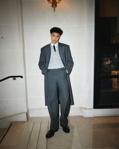 a man wearing a suit and tie standing in front of a door with his hands in his pockets