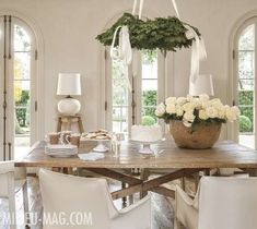 a dining room table with white chairs and flowers in a basket on top of it