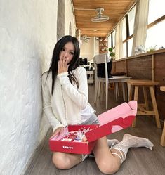 a woman sitting on the floor with a box in front of her, holding it up to her mouth