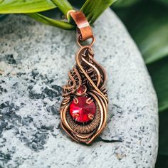 Copper Wire Wrapped Red Crystal Pendant. Handmade copper wire wrapped pendant necklace featuring a red crystal and accented with a red flat back cabochon. The pendant has been antiqued and polished, giving it an antique look. The size is about 3" in height by 1" width. One of a kind. Does not come with a chain. Embrace the fiery energy of this unique, handmade copper wire wrapped pendant necklace. The radiant red crystal is elegantly encased in hand-shaped copper wire, accented by a vibrant red Unique Red Copper Necklace, Unique Adjustable Copper Crystal Necklaces, Copper Amulet Round Pendant Jewelry, Adjustable Copper Amulet Jewelry, Red Amulet Pendant, Red Flats, Hand Shapes, Red Crystals, Handmade Copper