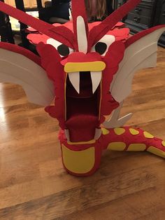 a red dragon made out of cardboard sitting on top of a wooden floor with its mouth open