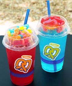 two plastic cups filled with different types of candy on top of a black table next to each other