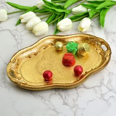 there is a gold tray with flowers on it and some green leaves next to it