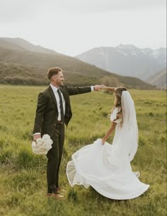 a bride and groom in the mountains pointing at each other