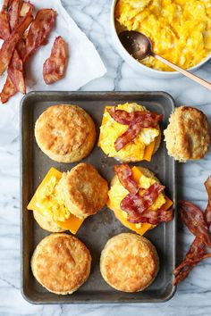 breakfast muffins with bacon and scrambled eggs on a baking sheet next to a bowl of macaroni and cheese