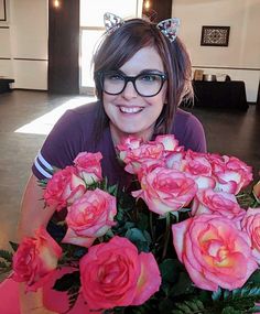 a woman wearing glasses holding a bouquet of pink roses in front of her face and smiling at the camera