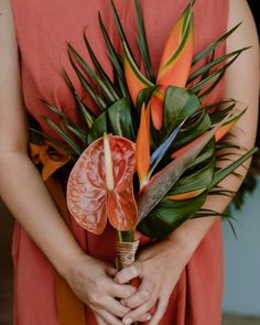 a woman in an orange dress is holding a bouquet with flowers and leaves on it