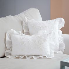 two white pillows sitting on top of a bed next to a pillow with ruffled edges