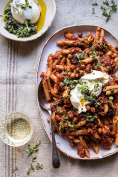 a white plate topped with pasta and meat covered in sauce next to a bowl of sour cream