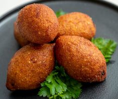 four fried food items on a black plate with parsley garnish around them