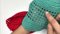 someone crocheting the sides of a green and red bag with their fingers on it