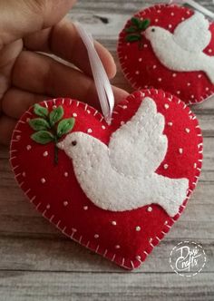 two red heart shaped ornaments with white doves on them are being held by someone's hand