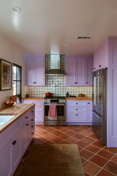 a kitchen with purple cabinets and tile flooring in the center, along with a stainless steel refrigerator