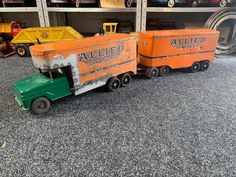 an orange and green toy truck on the ground next to other toys in a garage