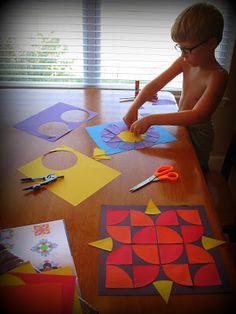 a young boy cutting out paper with scissors and glue on a table in front of some cut outs