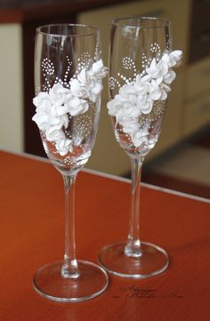 two wine glasses with flowers on them sitting on a wooden counter top next to each other