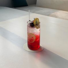 a tall glass filled with red liquid and topped with a lemon slice next to a straw