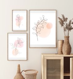 three framed art prints on the wall above a wooden cabinet with vases and flowers