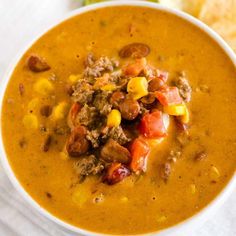 a close up of a bowl of soup with meat and corn on the side next to some bread