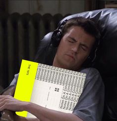 a man sleeping on a chair holding a yellow piece of paper over his face with headphones