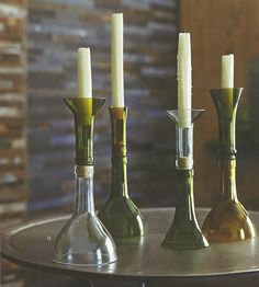 three bottles with candles in them sitting on a table next to two wine glasses and a candle holder