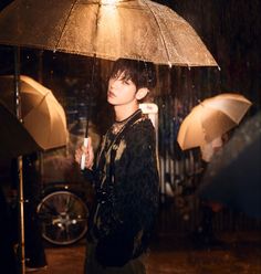 a person standing under an umbrella in the rain with other people behind them holding umbrellas