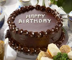 a chocolate cake with the words happy birthday written on it, surrounded by bread and flowers