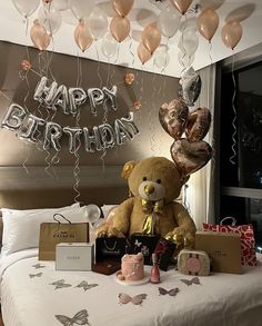 a teddy bear sitting on top of a bed surrounded by balloons and gifts in front of a happy birthday sign