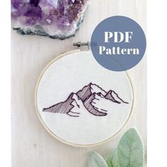 a hand embroidered mountain scene with the words pdf pattern on it next to some plants