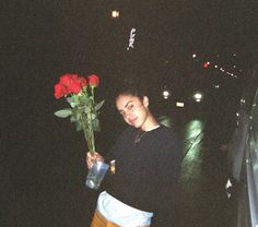 a woman holding a bouquet of red roses in her left hand while standing next to a car