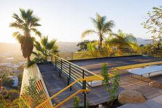 an outdoor tennis court surrounded by palm trees and yellow railings with benches on the side