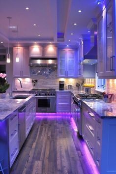 a kitchen with white cabinets and purple lights on the counter tops, along with an island