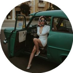 a woman sitting in the driver's seat of an old green car with her legs crossed