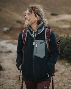 a woman wearing a blue jacket and carrying a brown backpack on her back walking down a dirt road