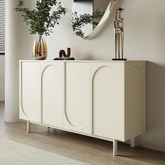 a white sideboard with two mirrors and plants on it in front of a window