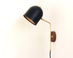 a black lamp on a white wall next to a wooden light fixture with a gold arm