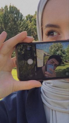 a woman taking a selfie with her cell phone in front of her face while wearing a headscarf