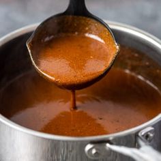 a ladle full of sauce being stirred by a wooden spoon in a metal pot