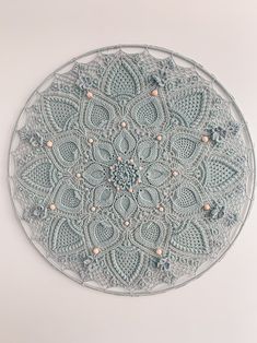 a circular doily made with crochet and beads on a white wall background