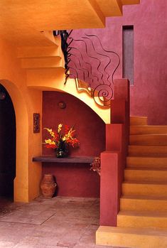 an entry way with stairs and vases on the table in front of red walls