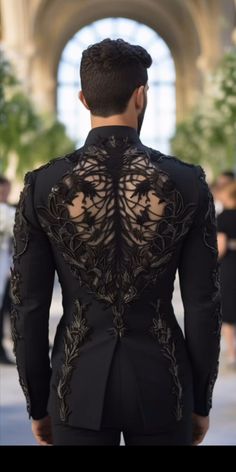 the back of a man wearing a black suit with gold embroidery on his chest and shoulders