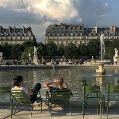 two women sitting on lawn chairs in front of a fountain with fountains and buildings in the background