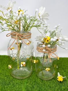 two mason jars with daisies tied to them on the grass next to each other